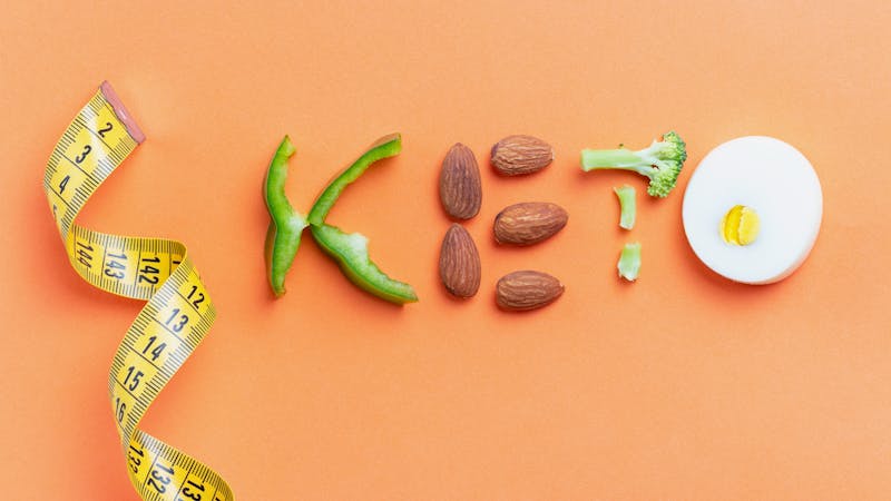 Inscription keto composed of vegetables and measuring tape on orange background