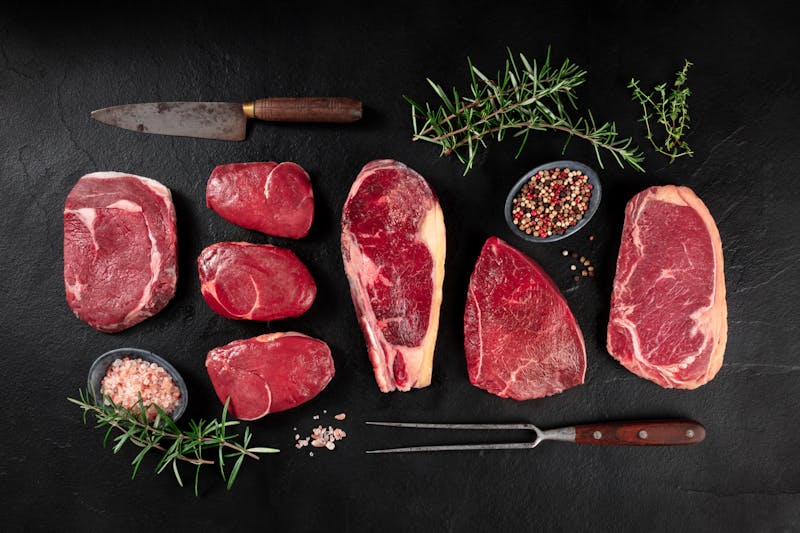 Meat, various cuts, overhead flat lay shot with a knife, a barbecue fork, salt, pepper, and rosemary