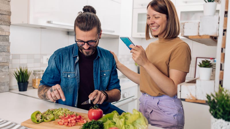 Young man making vegan dinner and his girlfriend helping him with the recipe