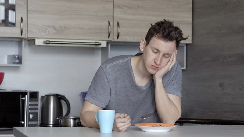 Beautiful sleepy man having breakfast at the table.
