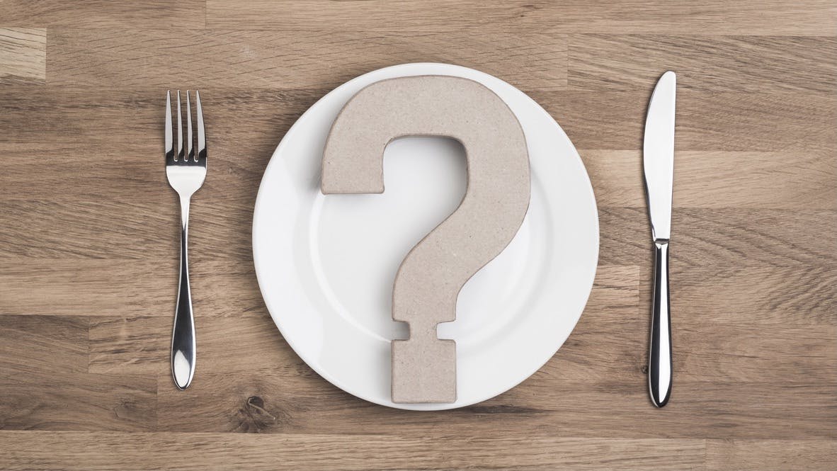 Overhead question mark on White plate with knife and fork on wooden table top
