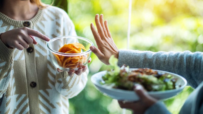 Women choosing to eat vegetables salad and making hand sign to refuse potato chips