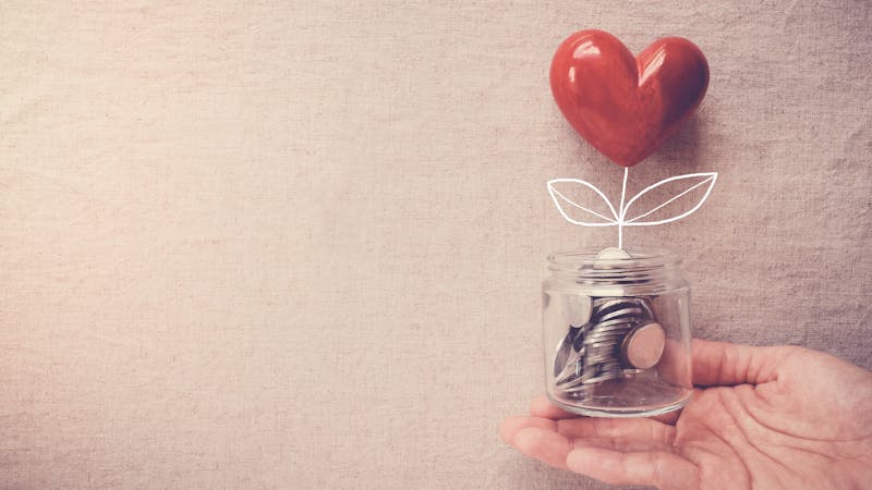 Hand holding a jar of heart tree growing on money coins, social responsibility and donation concept