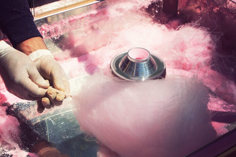 A person in latex gloves making pink cotton candy on a stick