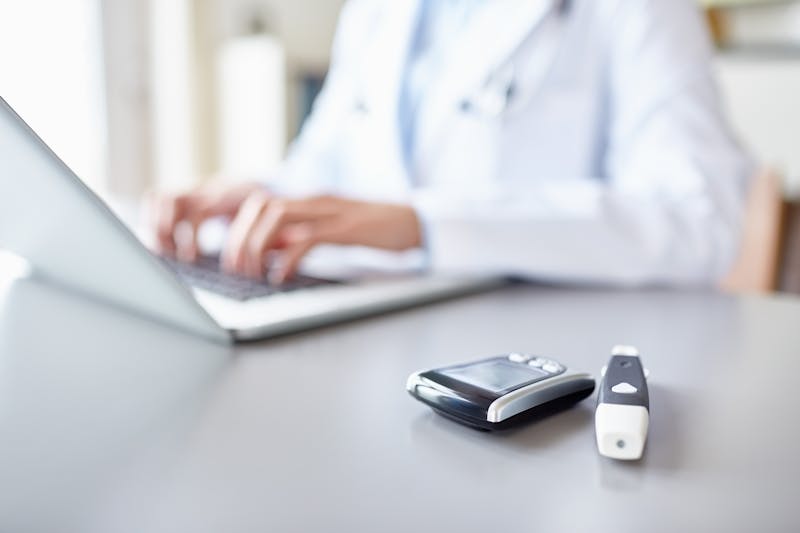 Glucometers on desk with doctor using laptop in background