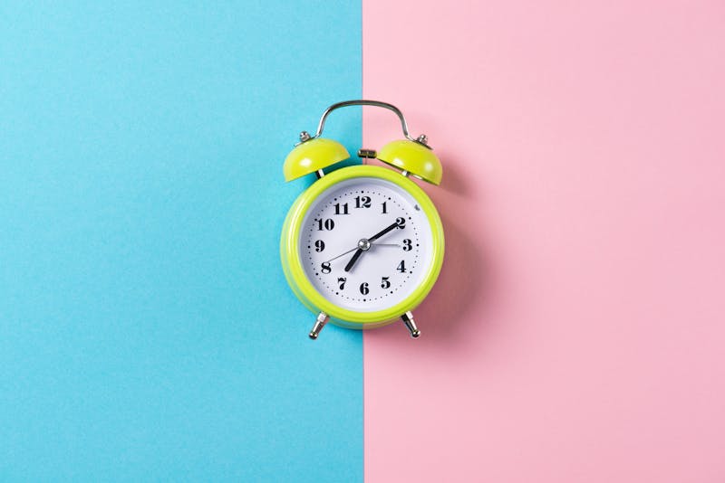 Green alarm clock with bells on blue and pink background, top view with copy space