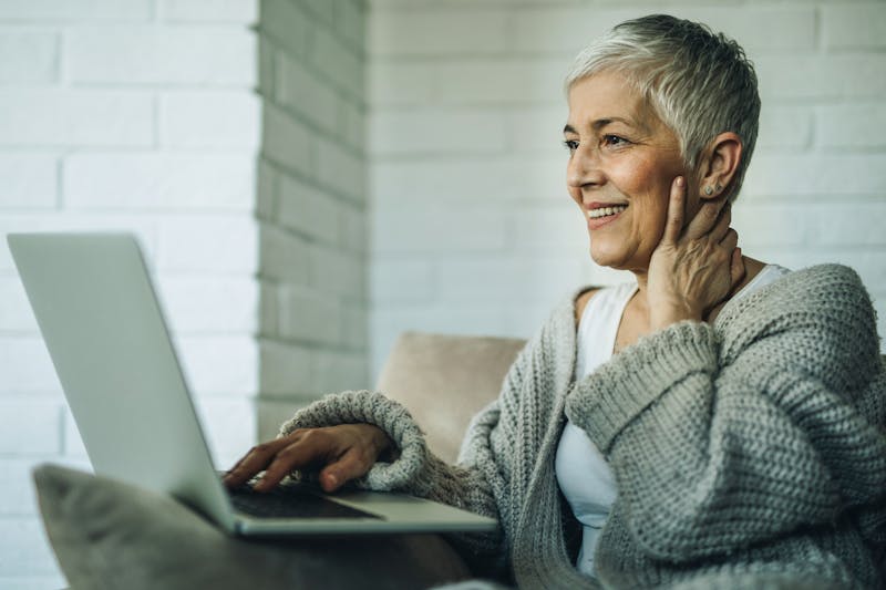 Happy senior woman using laptop while relaxing at home.