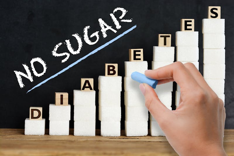 No sugar advice handwritten on blackboard above sugar cubes scale, suggesting diabetes risk