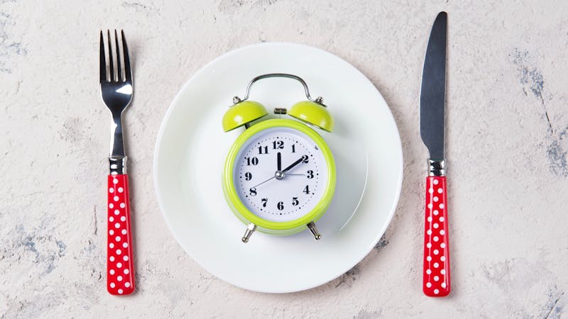 Alarm clock with bells on the plate with fork and knife, lunch time concept, top view with copy space