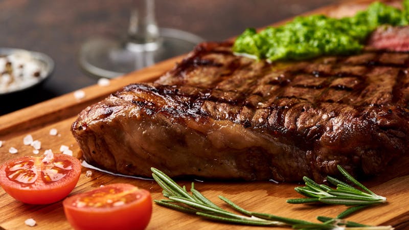 Grilled Black Angus Steak with tomatoes, garlic with chimichurri sauce on meat cutting board.