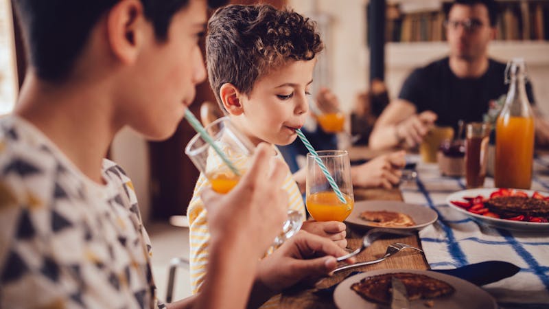 Boys drinking fresh orange juice during breakfast with family