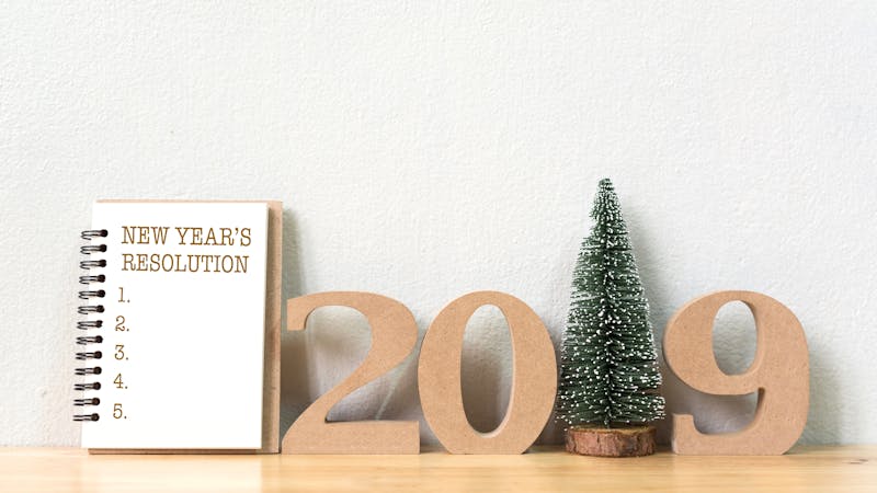 New year's resolution on a notebook and wood number 2019 with christmas tree on wood table and copy space