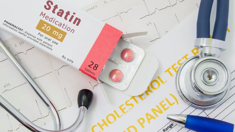 Effects and treatment of statins concept photo. Open packaging with drugs tablets, on which is written "Statin Medication", lies near stethoscope, result analysis on cholesterol (lipid panel) and ECG