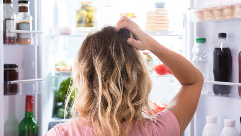 Confused Woman Looking In Open Refrigerator