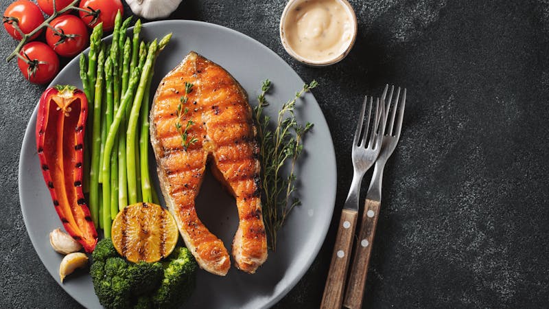 Tasty and healthy salmon steak with asparagus, broccoli and red pepper on a gray plate. Diet food on a dark background with copy space. Top view. Flat lay