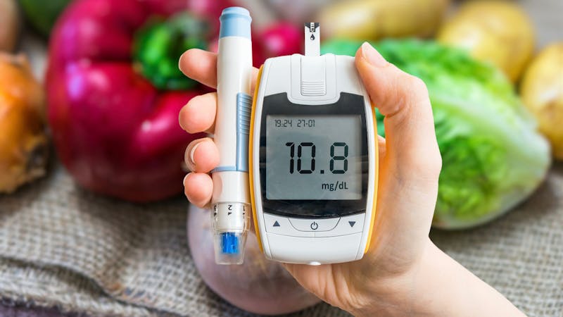 Diabetic diet, diabetes concept. Hand holds glucometer. Vegetables in background.