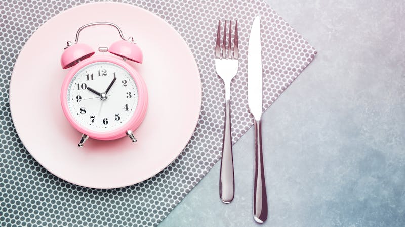 Alarm clock and plate with cutlery. Concept of intermittent fasting, lunchtime, diet and weight loss