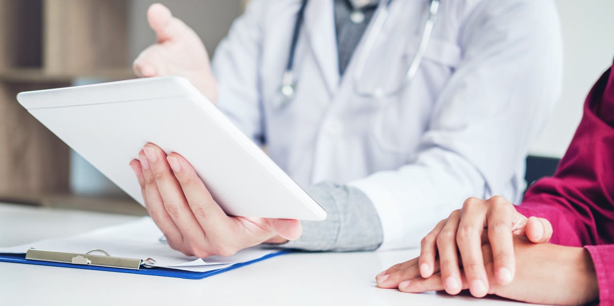 Doctor consulting with patient presenting results on digital tablet tablet  sitting at table