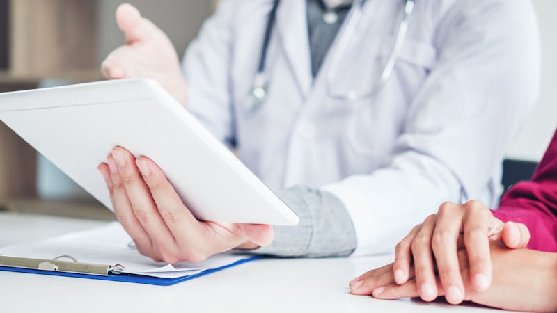 Doctor consulting with patient presenting results on digital tablet tablet  sitting at table