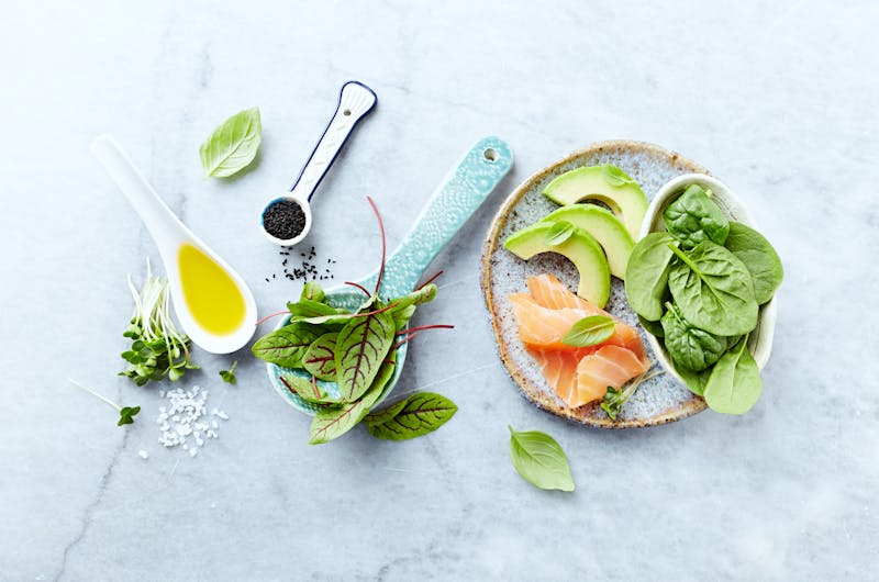 Ingredients for a healthy salad on gray stone background. Smoked salmon, avocado, spinach, sorrel, radis sprouts, black cumin. Flat lay. Healthy diet. Symbolic image.