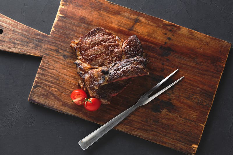 Rib eye steak on wooden board, top view