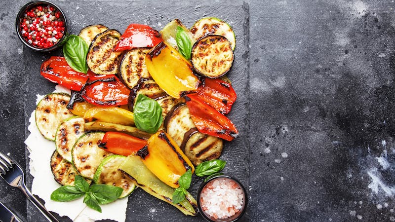 Grilled multicolored vegetables, aubergines, zucchini, pepper with green basil on serving stone board