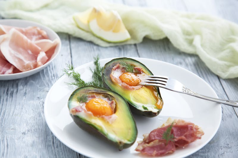 Two baked avocado halves with egg on a white saucer. Healthy Breakfast for the keto diet