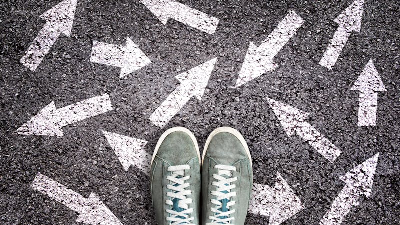 Sneaker shoes and arrows pointing in different directions on asphalt ground, choice concept