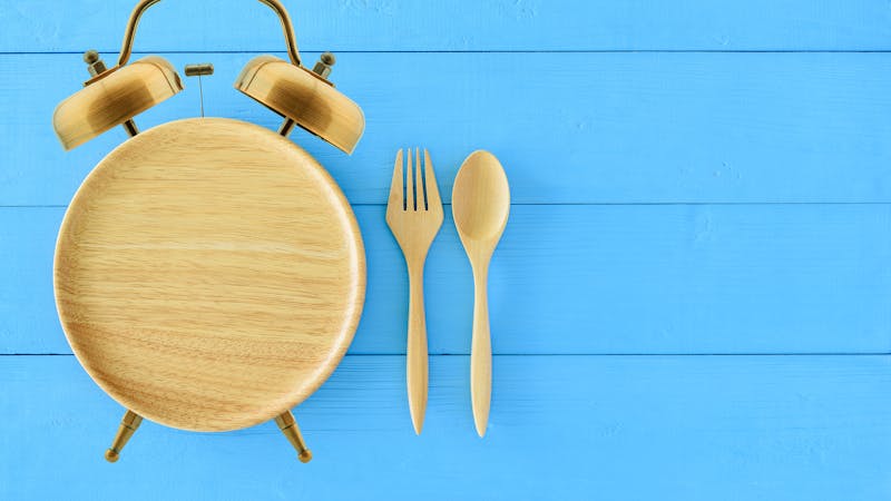 Intermittent fasting, diet and weight loss concept : Clock shaped wood dish, spoon and fork. Eco-friendly plate / kitchen utensil as alarm clock with ringing bell, depict alert or reminder time to eat