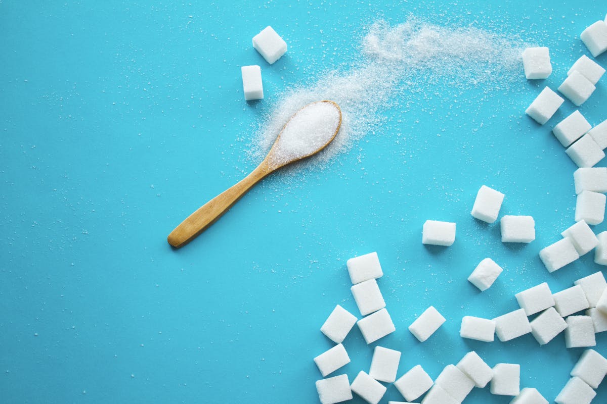 White sugar with spoon on blue background.
