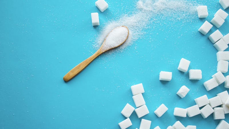 White sugar with spoon on blue background.