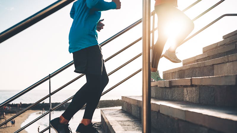 View of runners legs training outdoor – Young couple doing a workout session on stairs next the beach at sunset – Healthy people, jogging and sport lifestyle concept