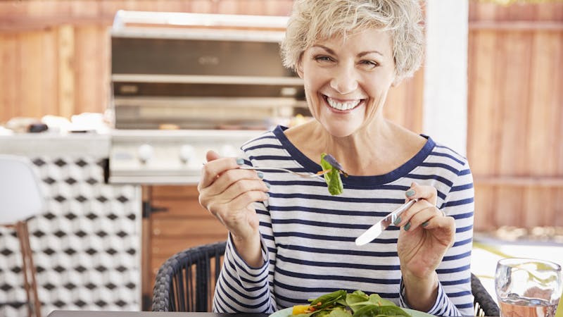 Senior white woman eating lunch at a table in her garden