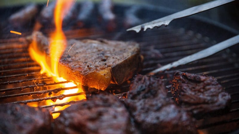 Flame Grilled Steaks Being Flipped On Barbecue With Tongs