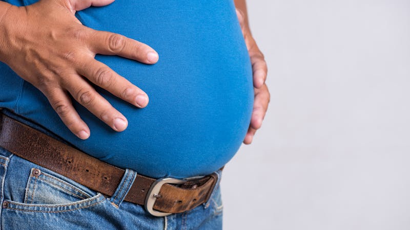 Overweight or fat adult man in very tight jeans on a gray background. Healthcare, medicine concept.