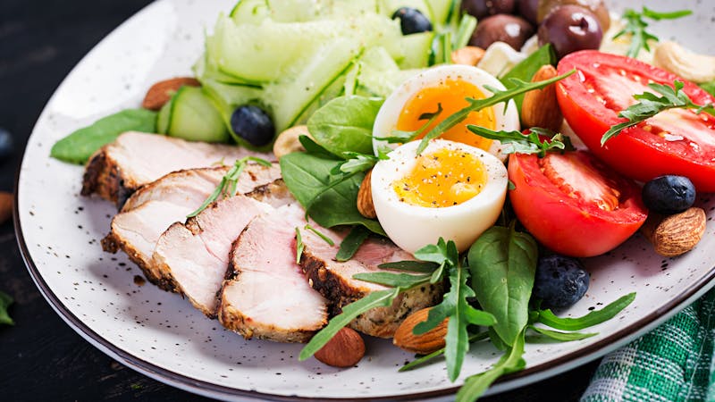 Ketogenic diet. Keto brunch. Boiled egg, pork steak and olives, cucumber, spinach, brie cheese, nuts and tomato.