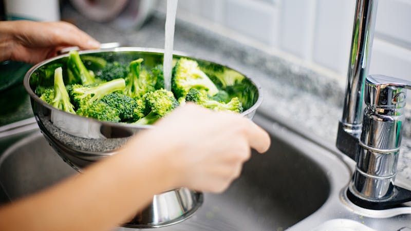 Woman washing broccoli in the kitchen sink