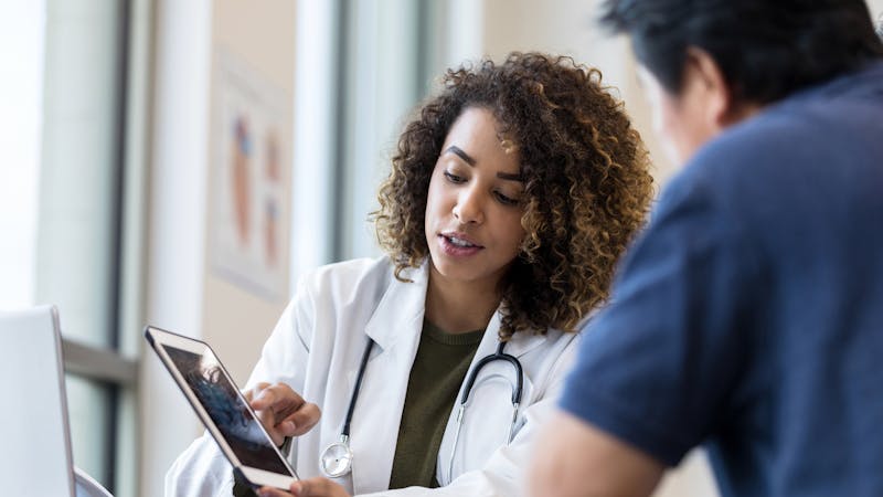 Female doctor uses tablet to show x-ray to senior man