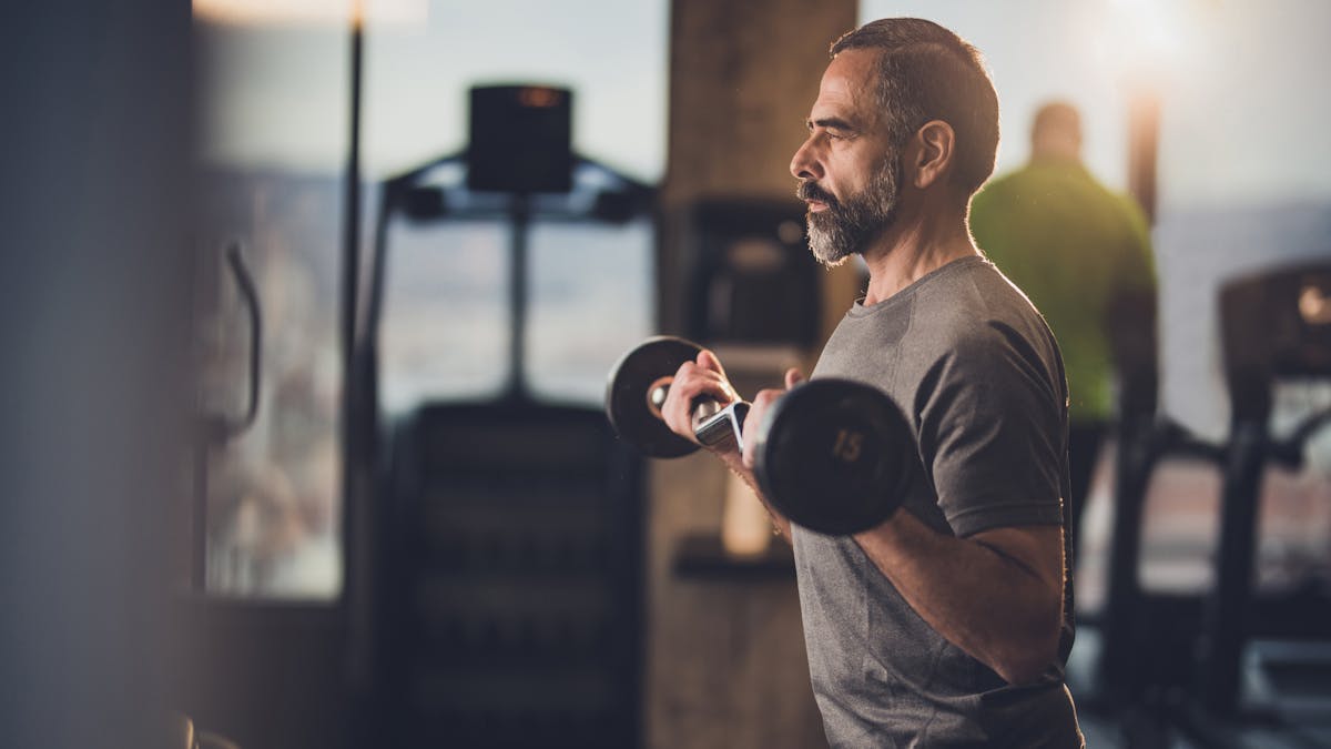 Active senior man having strength exercise with barbell in a gym.