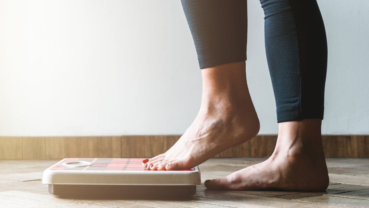 Female checking kilogrammes getting on the scale – self care and body positivity concept – warm flare on left