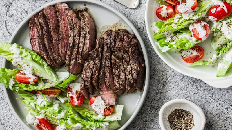 Beef medium rare steak and romaine salad cherry tomatoes yogurt dressing salad on a gray background, top view