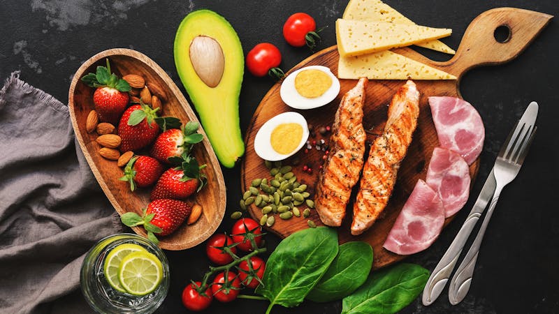 Grilled salmon with boiled egg, ham, vegetables and strawberries on a dark background. Keto diet dinner or lunch. Top view, flat lay.