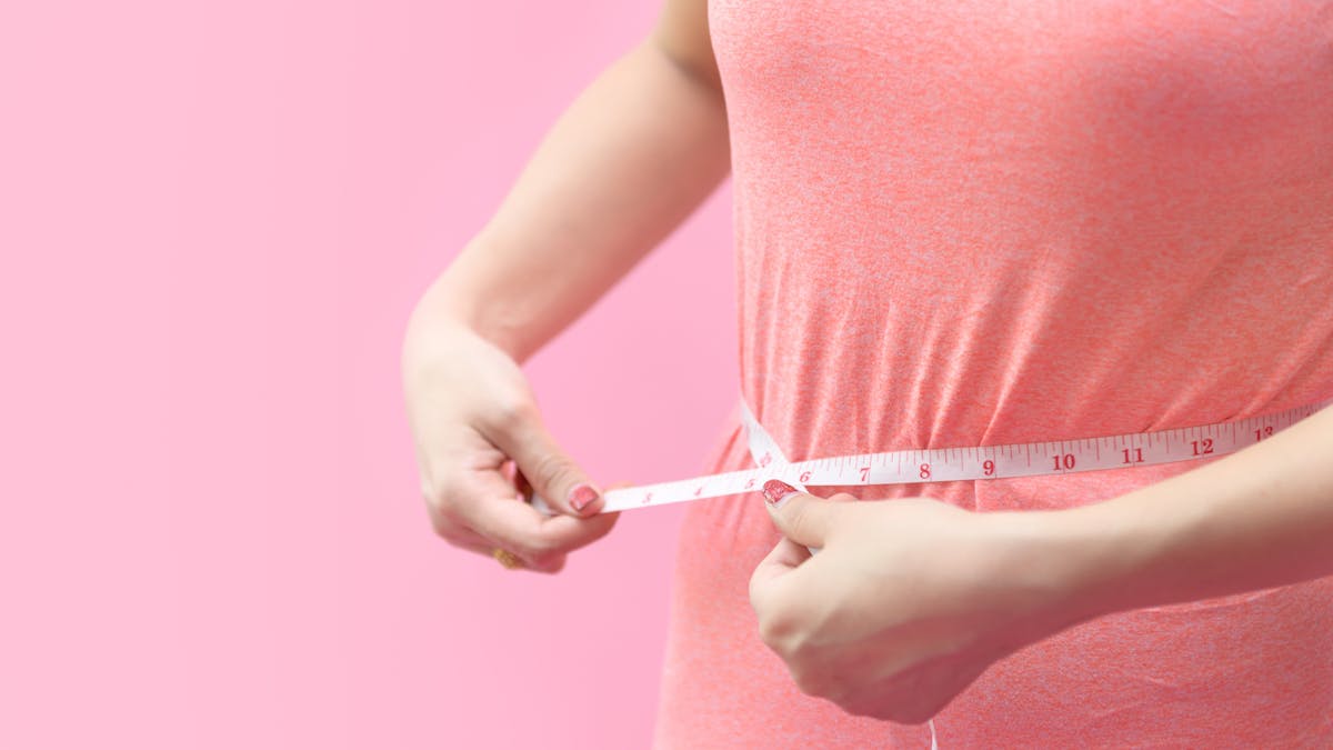 Cute young woman measuring her waist isolated on pink