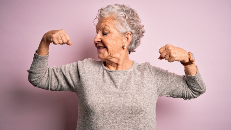 Senior beautiful woman wearing casual t-shirt standing over isolated pink background showing arms muscles smiling proud. Fitness concept.