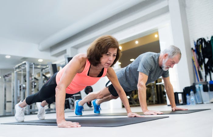 Senior couple in gym working out, doing push ups