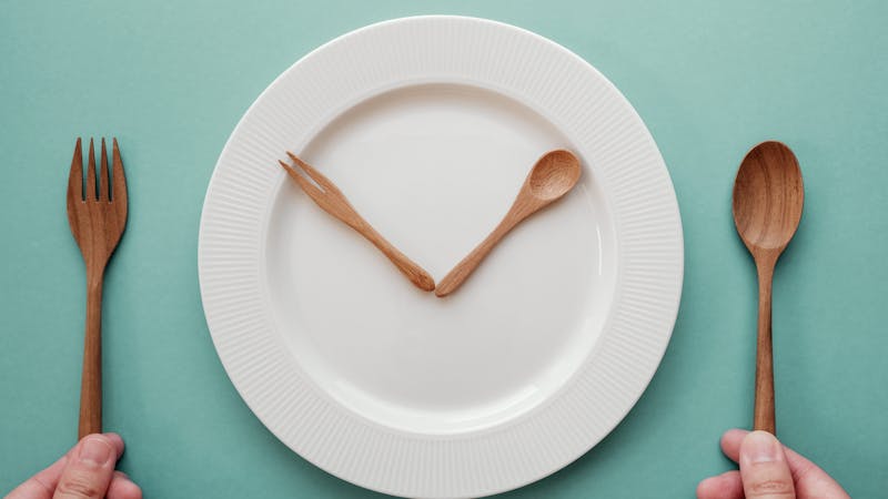 wooden spoon and fork as a clock hands on white plate, Intermittent fasting concept, ketogenic diet, weight loss, skip meal
